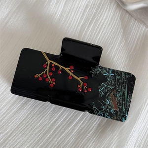 Detail of elegant black hair claw clip with golden plum blossom and bamboo pattern