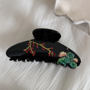 Detail of glossy black acetate hair claw clip featuring painted lotus and red rhinestones