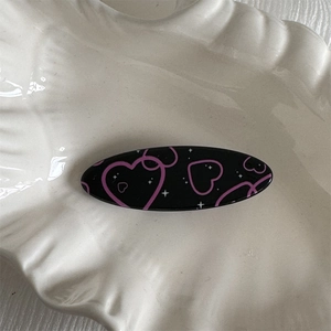 Detail of oval black hair clip with pink heart pattern on a shell ceramic tray