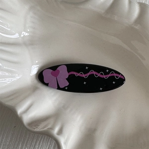 Detail shot of a sweet black oval hair clip with pink bow patterns on a ceramic plate