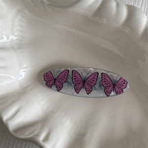 Close-up of acetic acid hair clip with pink butterfly patterns on a white shell tray