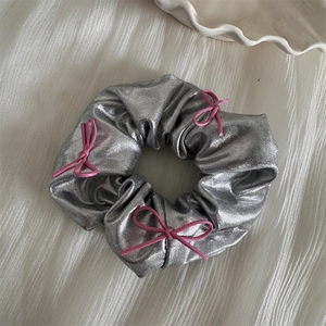 Detail of silver metallic scrunchie featuring decorative small pink string bows
