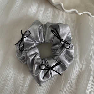 Detail of silver metallic scrunchie with delicate black ribbon bows on textured white fabric