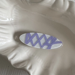 Close-up of glitter oval hair clip with purple ribbon bow design on shell tray
