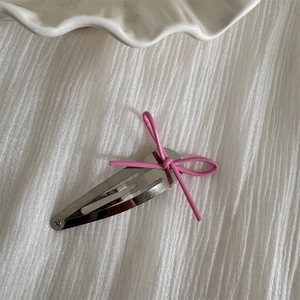 Detail of a pink string bow on a silver teardrop hair clip against a soft white fabric