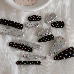 Detail of colorful polka dot hair clips in various shapes on a textured white fabric background