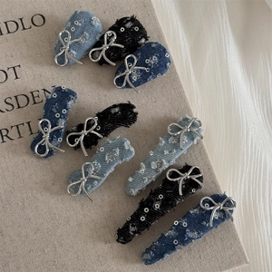 Close-up of denim hair clips with silver sequins and metallic bow charms on fabric