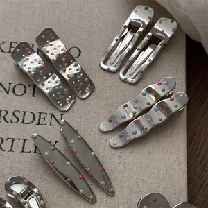 Detail of silver geometric hair clips with colorful dots on a textured beige surface
