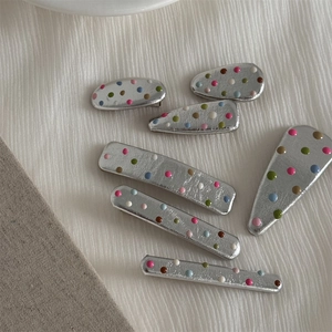 Close-up of seven silver hair clips with colorful polka dots on white fabric