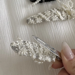 Detailed view of cream lace hair clip with embroidery texture and metal duckbill base