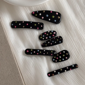 Close-up of black hair clips with 3D colorful macaron polka dots on white fabric
