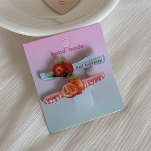 Dettaglio di fermagli per capelli a tema frutta con motivi a quadri blu e righe rosa