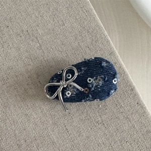 Close-up of denim hair clip featuring silver bow and sequins on blue fabric