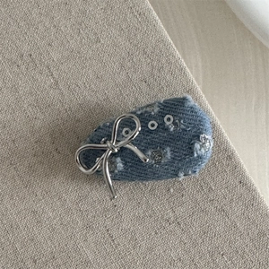 Detail of blue denim hair clip featuring a silver metal bow and glitter sequins decoration