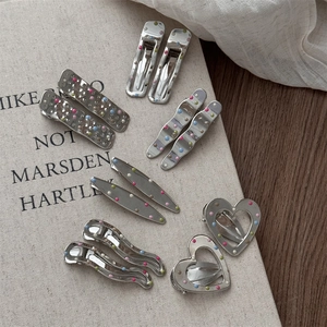 Variety of silver metal hair clips with colorful polka dots on a textured book surface