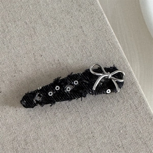 Detail of silver bow and sequins on distressed black denim hair clip with frayed edges