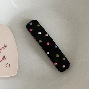 Detail shot of a black rectangular hair clip with colorful 3D dots on a grey textured surface