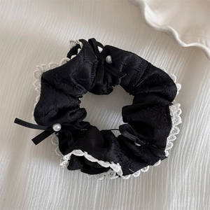 Detailaufnahme eines schwarzen Scrunchie mit Spitzenrand, weißen Perlen und Schleife