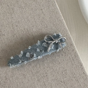 Detail of light blue denim hair clip with silver bow and sequins on burlap background