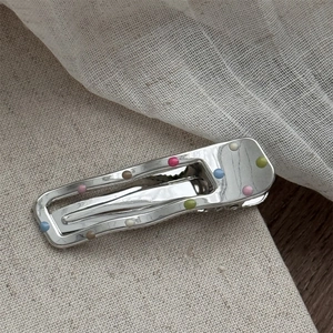 Detail view of silver metal hair clip with colorful polka dots on a soft fabric background