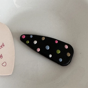 Detail view of colorful 3D resin polka dots on a black leather-based BB hair clip