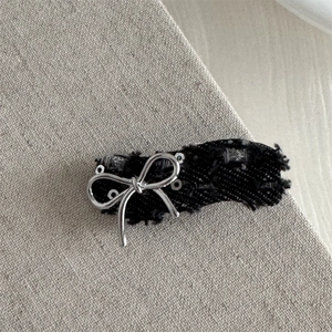 Detail of denim bow hair clip with silver studs and frayed edges on grey background