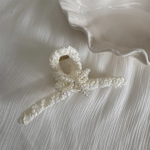 Detail of cream white knitted hair claw clip featuring elegant pearl bow embellishments