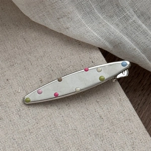 Close-up of silver metal hair clip with colorful enamel polka dots on linen background