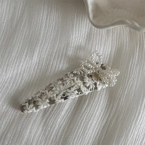 Detail of elegant lace hair clip with artificial pearl bow on a white textured fabric
