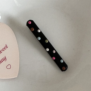 Detail showing a black fabric hair clip with colorful multi-colored 3D polka dot beads