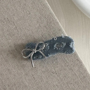 Detail of a denim hair clip with a silver metallic bow and sequins on beige fabric