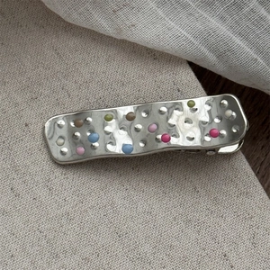 Detailed close-up of a silver hammered metal hair clip with colorful enamel dots on fabric