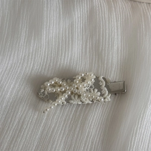 Detailed view of elegant white lace bow hair clip with pearls on silver metal base