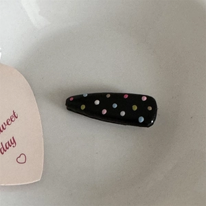 Close-up of black hair clip featuring colorful rainbow polka dots on a neutral background
