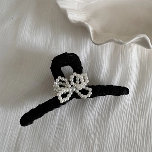 Detail of elegant black fabric hair claw clip with white faux pearl bow decoration