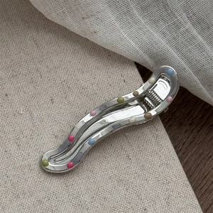 Close-up of wavy silver metal hair clip with colorful enamel dots on textured fabric