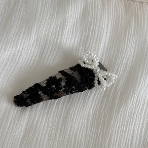 Close-up of black floral lace hair clip featuring a delicate white pearl bow accent