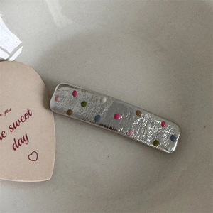 Close-up of silver rectangular hair clip with colorful polka dots and hammered texture