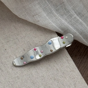 Macro view of silver wave hair clip with colorful polka dots on beige fabric