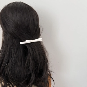 Pince à cheveux élégante avec double nœud blanc portée sur des cheveux bouclés foncés