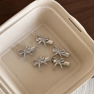Détail de 5 petites barrettes nœuds en métal argenté sur un fond rustique texturé