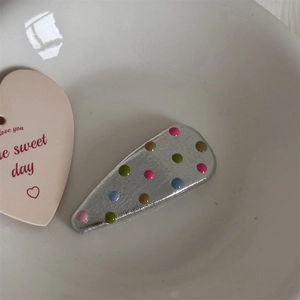 Macro shot of silver metal hair clip with colorful 3D polka dots in a white bowl