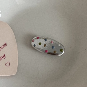 Detailed view of silver oval hair clip featuring colorful rainbow polka dot patterns