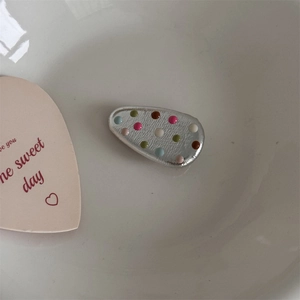 Detailed close-up of a silver hair clip with colorful 3D dots in a white ceramic dish