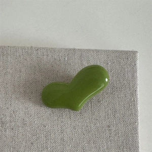 Detailansicht einer herzförmigen Haarklammer in Avocadogrün auf Leinentextur