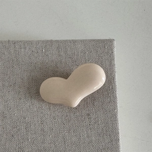 Detailaufnahme der herzförmigen beigen Haarklammer mit glänzendem Keramik-Finish