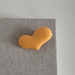 Nahaufnahme einer leuchtend orangefarbenen Herz-Haarklammer auf grauem Stoffhintergrund