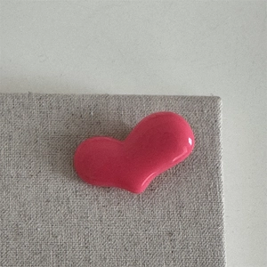 Detail einer glänzenden pfirsichrosa herzförmigen Haarspange auf strukturiertem Leinen