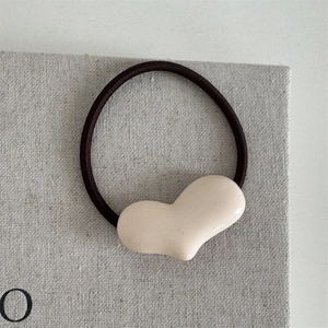 Detail einer minimalistischen cremefarbenen Herz-Haarklammer mit schwarzem Gummiband