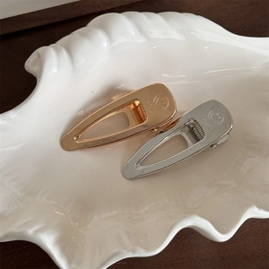 Close-up of gold and silver metallic smile duckbill hair clips on a ceramic tray